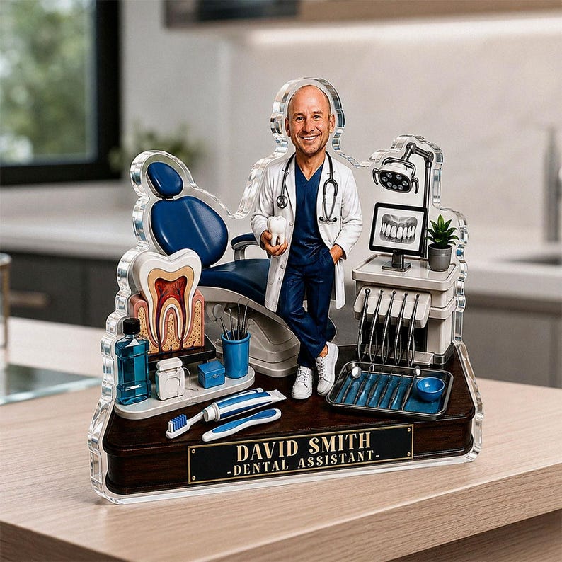 May include: A custom acrylic figurine of a dental assistant in a white coat and blue scrubs, standing next to a dental chair, a tooth model, dental tools, and a monitor. The base features a plaque with the text DAVID SMITH - DENTAL ASSISTANT.