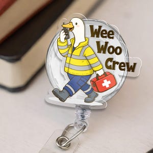 May include: A clear, round retractable badge reel featuring a cartoon duck in a yellow and gray safety jacket, blue pants, and gray boots. The duck is holding a walkie-talkie and a red first aid kit. The text "Wee Woo Crew" is displayed.