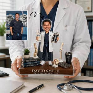 May include: A custom acrylic bobblehead of an orthopaedic surgeon wearing a white coat and navy scrubs, standing on a wooden base labelled DAVID SMITH ORTHOPAEDIC SURGEON. The display includes miniature anatomical models, books, and a medical tray.