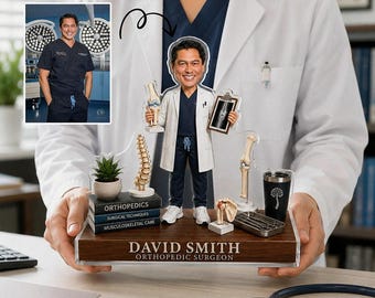 May include: A custom acrylic bobblehead of an orthopaedic surgeon wearing a white coat and navy scrubs, standing on a wooden base labelled DAVID SMITH ORTHOPAEDIC SURGEON. The display includes miniature anatomical models, books, and a medical tray.