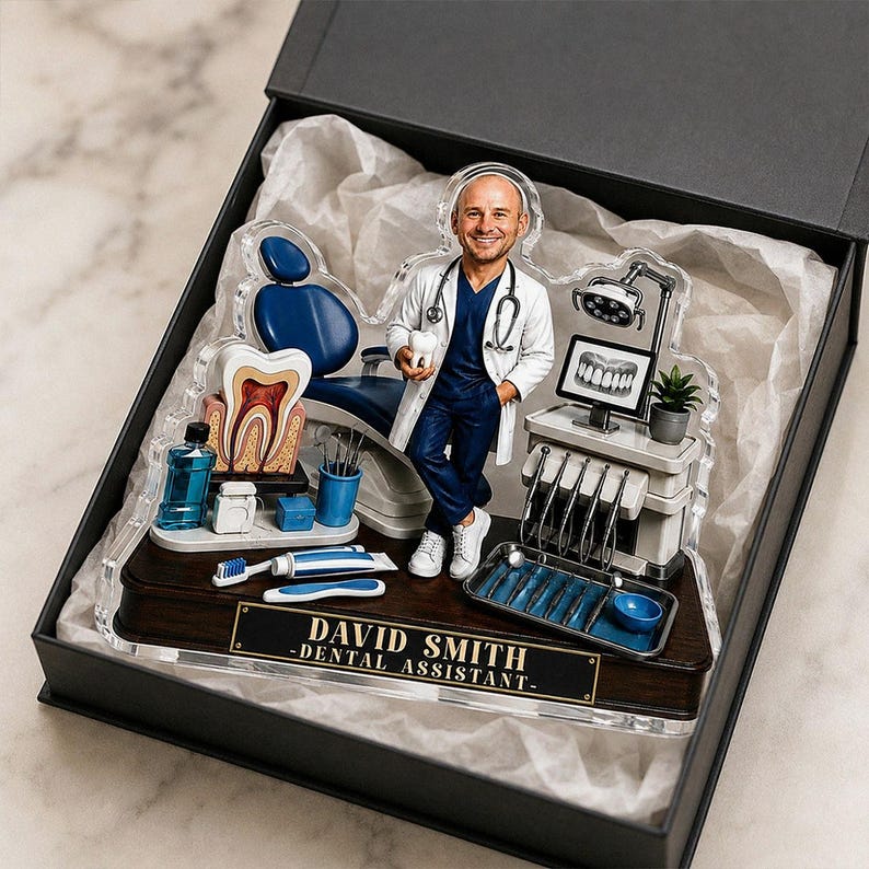 May include: A custom acrylic desk ornament featuring a dental assistant figurine, a blue dental chair, a tooth model, and dental tools. The base is dark wood with a gold plaque reading DAVID SMITH -DENTAL ASSISTANT- inside a black gift box.