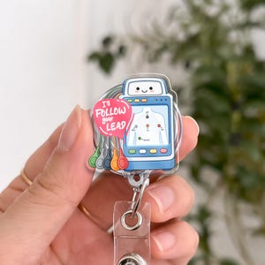 May include: A clear badge reel with a medical theme. The badge features a smiling ultrasound machine with a human figure diagram. A pink speech bubble reads "I'll follow your lead." Attached are colorful ECG leads.