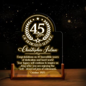 May include: A lighted acrylic award for 45 years of dedicated service. The design features a gold laurel wreath, stars, and the text "45 Years of Dedicated Service" with the name "Christopher Julian" and a congratulatory message.