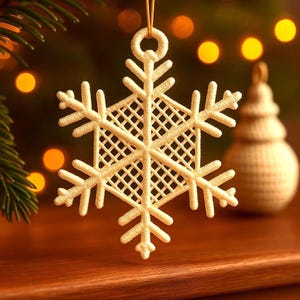 May include: Cream-colored snowflake Christmas ornament with a delicate, openwork design. The snowflake is suspended by a gold string, with a blurred background of Christmas lights and a small tree ornament. The ornament is approximately 4 inches in diameter.