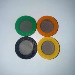 May include: Four circular filters with mesh centres and coloured rims. The colours are green, orange, black, and yellow. The filters are arranged in a square formation against a white background.