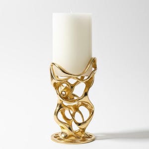 May include: A gold-colored, abstract candle holder with a white pillar candle. The candle holder has an open, organic design with a round base. The candle is a standard size, and the holder is made of a shiny metal.