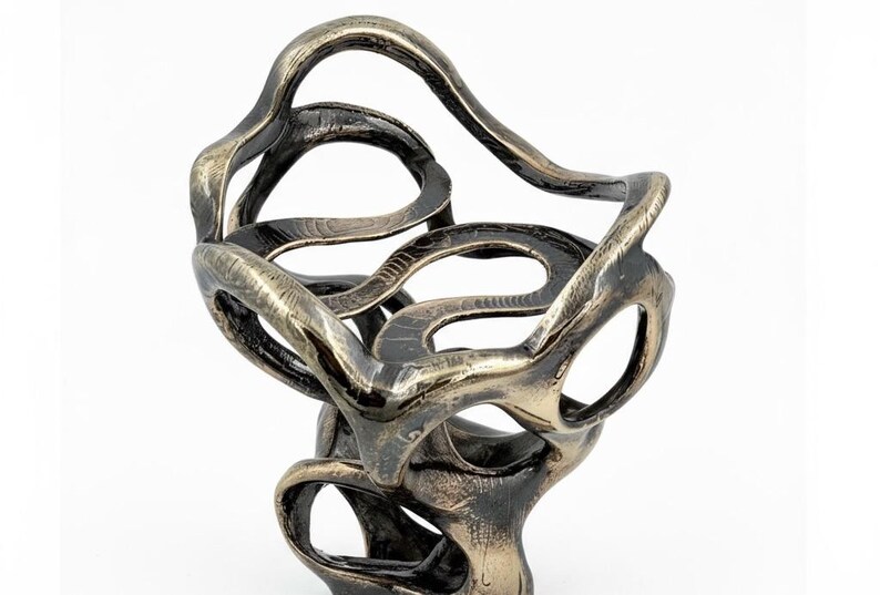 May include: Abstract bronze sculpture with a swirling, open design. The sculpture features interconnected loops and curves, creating an organic, flowing form. The metallic finish has a mix of bronze and dark tones, adding depth and visual interest.