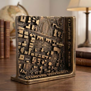 May include: A bronze-toned metal sculpture featuring a raised, three-dimensional map of the Stanford University campus. The piece includes the text "CLASS OF 2018" vertically on the right side and "STANFORD UNIVERSITY" along the bottom edge.