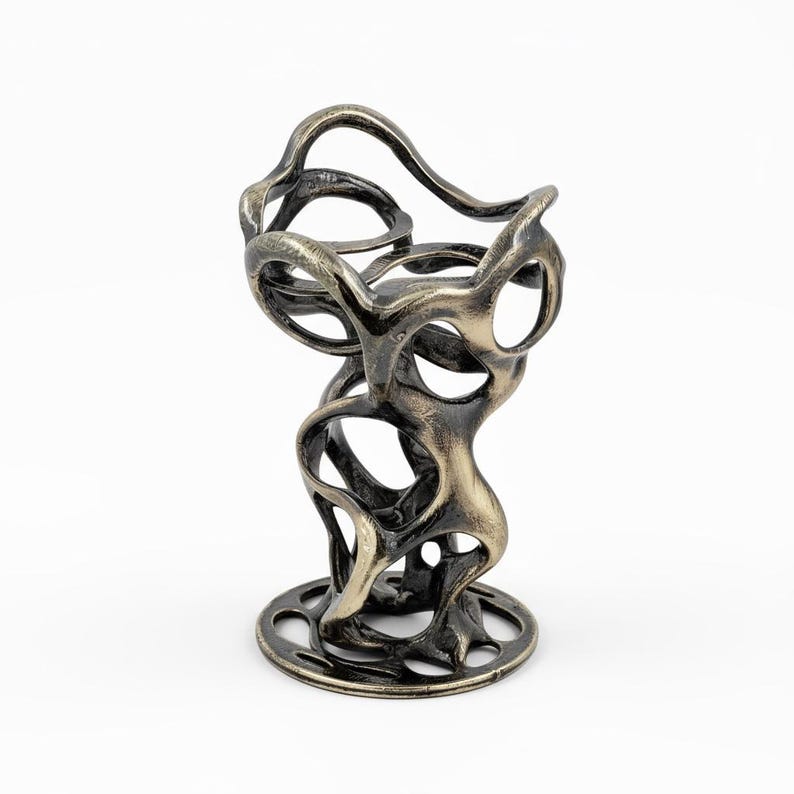 May include: An abstract bronze-colored sculpture with a circular base and an open, flowing design. The sculpture features interconnected, organic shapes with multiple openings, creating a unique and artistic aesthetic. The metal has a textured finish.