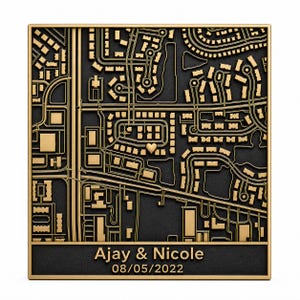 May include: A square wall plaque featuring a raised gold-colored street map on a textured black background. A small gold heart marks a specific location on the map. The bottom section displays the text Ajay & Nicole and the date 08/05/2022.