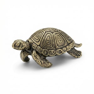 Peut inclure: Une figurine de tortue en bronze détaillée, avec une carapace texturée et des détails complexes. La tortue est représentée en position de marche, la tête et les pattes tendues. La figurine est posée sur un fond blanc.