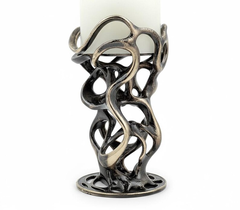 May include: A decorative candle holder with a unique, openwork design. The metal holder has a dark bronze finish with lighter bronze accents. A white candle sits in the center of the holder. The base is round with a decorative pattern.