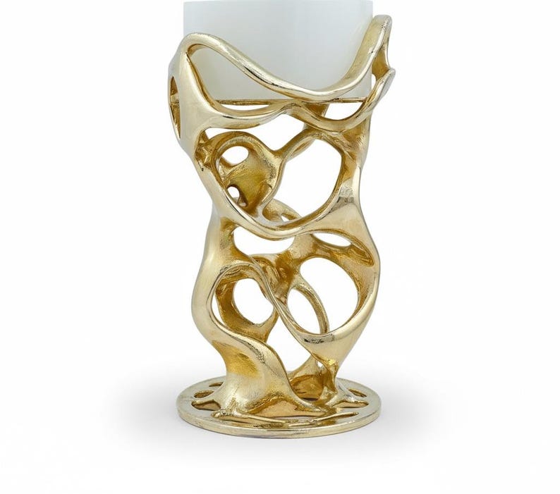 May include: A gold-colored, abstract candle holder with a white candle. The holder has an open, organic design with a circular base. The candle is a square shape.