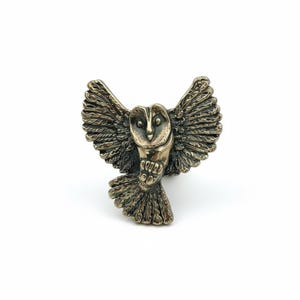 May include: A bronze owl figurine with its wings spread wide. The owl is depicted in flight, with detailed feathering and a focused expression. The figurine is a warm bronze colour and is set against a white background.