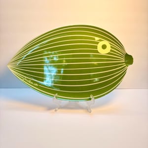May include: A leaf-shaped ceramic tray in a vibrant green color featuring thin, horizontal white stripes across its surface. The tray includes a circular white eye detail on the right side and the signature Jonathan Adler printed in white.