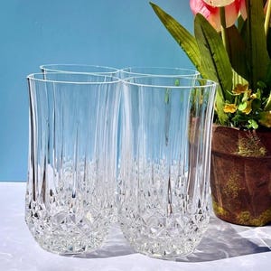 May include: A set of four clear glass tumblers featuring a vertical ribbed pattern on the upper portion and a textured diamond-cut design around the base. The glasses are transparent with a reflective surface, showcasing a clear, faceted glass construction.