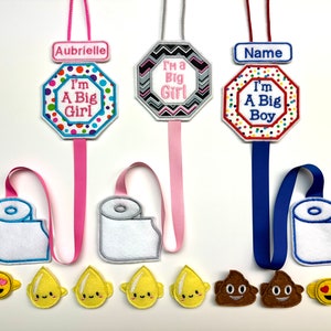 May include: Three personalized toilet paper holder decorations with embroidered designs. The top design features a white octagon with colorful polka dots and the text "I'm A Big Girl". The middle design features a black and white octagon with a chevron pattern and the text "I'm A Big Girl". The bottom design features a red octagon with colorful polka dots and the text "I'm A Big Boy".
