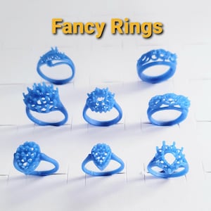 May include: A collection of eight blue wax ring models for jewelry casting, arranged in three rows. Each ring features intricate prong settings for gemstones. The text "Fancy Rings" is displayed in yellow at the top of the image.
