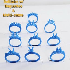 May include: A collection of blue wax ring models in various designs, including solitaire, baguette, and multi-stone settings. The rings are arranged on a white surface, showcasing different styles for jewelry design. The text "Solitaire w/ Baguettes & Multi-stone" is visible.