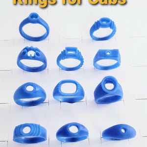 May include: A collection of eleven blue wax ring models for cabochons, arranged in rows. Each ring features a distinct setting style, including round, square, and oval mounts. The text "Rings for Cabs" is displayed in yellow at the top of the image.
