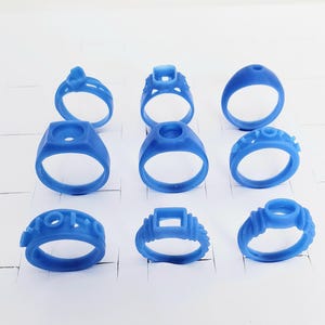 May include: A collection of nine blue wax ring models in various designs, ready for the jewelry-making process. The rings feature different shapes and details, showcasing the variety of potential designs.
