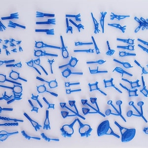 May include: A collection of blue jewelry wax models in various shapes, including ring settings, pendants, and decorative elements. The models are arranged on a white surface, showcasing the diversity of designs.