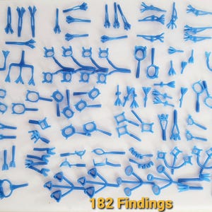 May include: A collection of 182 blue plastic jewelry findings arranged in a grid. The components include various prong settings, multi-pronged connectors, and branched structures, all featuring a smooth, uniform blue finish and intricate shapes.