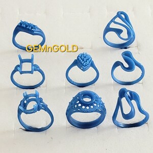 May include: Eight blue wax ring molds for jewelry making. The molds are arranged in three rows on a white surface. The molds are all different shapes and sizes. The text "GEMnGOLD" is visible in the image.