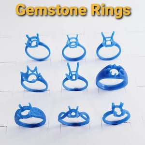May include: Nine blue gemstone ring molds are displayed on a white surface. The rings have various designs, with prongs and settings ready for gemstones. The text "Gemstone Rings" is in yellow at the top of the image.