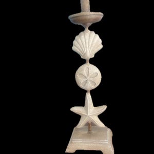 May include: A beige lamp with a seashell theme. The lamp features a base, a starfish, a sand dollar, and a seashell. The lamp is topped with a light fixture.