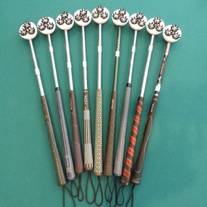 May include: Nine golf club training aids with black and white patterned grips and white heads with black spikes. The training aids are arranged in a semi-circle on a green surface.