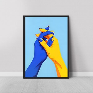 May include: A framed art print featuring two hands clasped together. One hand is painted blue, the other yellow, with matching nail polish. The background is a solid light blue color.