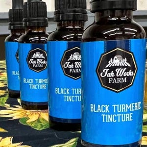 May include: Several brown glass bottles with black droppers and blue labels. The labels read "Tah Works Farm" and "Black Turmeric Tincture" in white text. The bottles are arranged in a row, suggesting a health product.