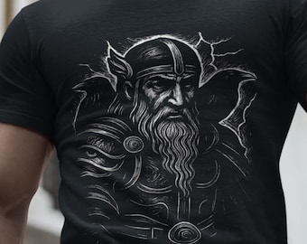 Könnte beinhalten: Schwarzes T-Shirt mit einer schwarz-weißen Illustration eines bärtigen Kriegers mit Helm und Rüstung. Das Design befindet sich auf der Brust. Die Person steht draußen vor einem weißen Gebäude.