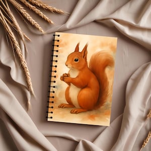 Op de afbeelding: Spiraalgebonden notitieboek met een aquarel illustratie van een rode eekhoorn. De eekhoorn is zittend afgebeeld, met de pootjes tegen elkaar. Het notitieboek heeft een zwarte spiraalbinding en een warm kleurenpalet.