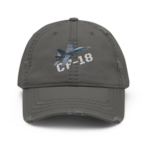 May include: Distressed gray baseball cap featuring a graphic of a CF-18 fighter jet. The text "CF-18" is printed in white on the front. The cap has a pre-worn look with distressed details.