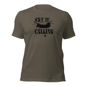 Könnte beinhalten: Olivgrünes T-Shirt mit dem Text "SKY IS CALLING" in verblichener schwarzer Schrift. Eine schwarze Helikoptergrafik befindet sich über dem Wort "CALLING". Das T-Shirt hat kurze Ärmel und einen Rundhalsausschnitt.