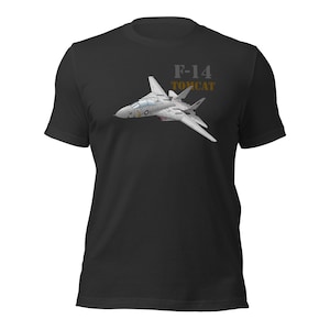 Może przedstawiać: Czarny t-shirt z krótkim rękawem z grafiką przedstawiającą szary myśliwiec F-14 Tomcat w locie. Napis F-14 TOMCAT jest nadrukowany szarymi i złotymi literami nad samolotem, który posiada małe niebiesko-białe oznaczenie na kadłubie.