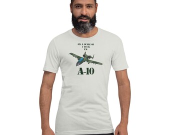 May include: A light gray t-shirt featuring a graphic of an A-10 Thunderbolt II aircraft. The text "ON A SCALE OF 1 TO 10, I'M" is above the aircraft, and "A-10" is below. The shirt is worn by a person.