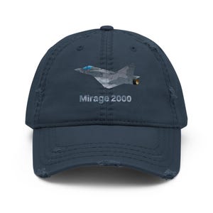 May include: Navy blue distressed baseball cap featuring a graphic of a Mirage 2000 fighter jet. The text "Mirage 2000" is printed below the jet. The cap has a pre-worn look with distressed edges.