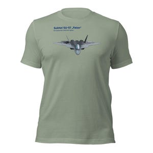 May include: A pale green t-shirt with a graphic of a Sukhoi SU-57 "Felon" fighter jet. The text "Sukhoi SU-57 Felon" and "5th Generation Multirole Fighter" are printed above the jet. The shirt has short sleeves and a crew neck.