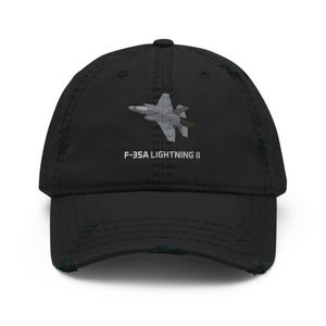 May include: Black distressed baseball cap featuring an embroidered image of an F-35A Lightning II fighter jet. The text "F-35A LIGHTNING II" is printed below the jet. The cap has a curved brim and a worn, vintage look.
