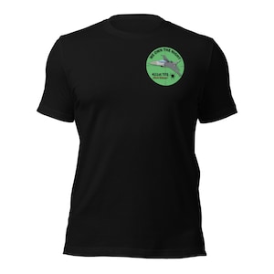 May include: Black t-shirt with a circular emblem showing a jet plane and the text "WE OWN THE NIGHT" and "421st TFS Black Widows". The emblem is green with white and grey details. The shirt is made of a soft material.