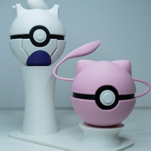 Op de afbeelding: Twee 3D-geprinte figuren, een witte en een roze, die op stripfiguren lijken. De witte figuur heeft een zwart-wit ontwerp met een blauw accent. De roze figuur heeft een zwart-wit ontwerp met een roze aanhangsel. Beide figuren staan op een witte basis.