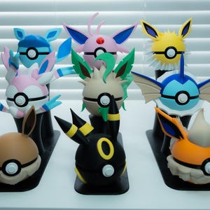 Peut inclure: Collection de figurines Pokémon colorées, chacune avec des designs et des caractéristiques uniques. Les figurines sont exposées sur des socles noirs, présentant une variété de personnages aux couleurs et formes différentes. Les figurines mesurent environ 7,6 cm de haut.