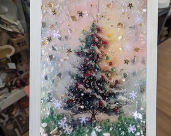 May include: A framed Christmas tree art piece. The artwork features a detailed evergreen tree adorned with red, green, and gold ornaments. The background has a mix of glitter, stars, and snowflakes, all encased in a white wooden frame.