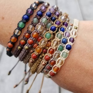 May include: A stack of colourful beaded bracelets with different coloured stones and cords. The bracelets are made with natural materials and have a bohemian style.