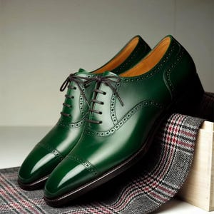 May include: A pair of polished, emerald green leather dress shoes with dark brown laces. The shoes feature a classic cap-toe design and decorative perforations. They rest on a gray and red plaid fabric, suggesting a focus on formal footwear.