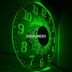 May include: A green illuminated wall clock with a decorative mandala design in the center. The clock face features large, stylized numerals and the text "ZEESTORE313". The clock is lit with a bright green light.