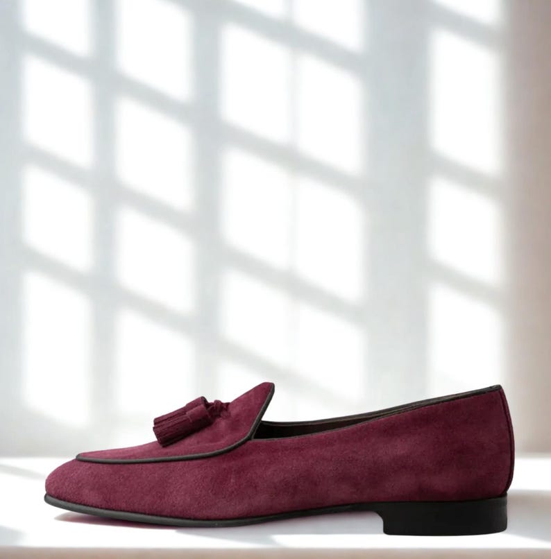 May include: A burgundy suede loafer with a tassel detail. The shoe has a rounded toe and a black sole. The shoe is approximately 11 inches long.